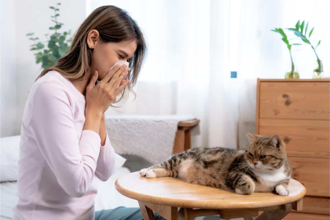 Woman sneezing with a cat sitting next to her.
